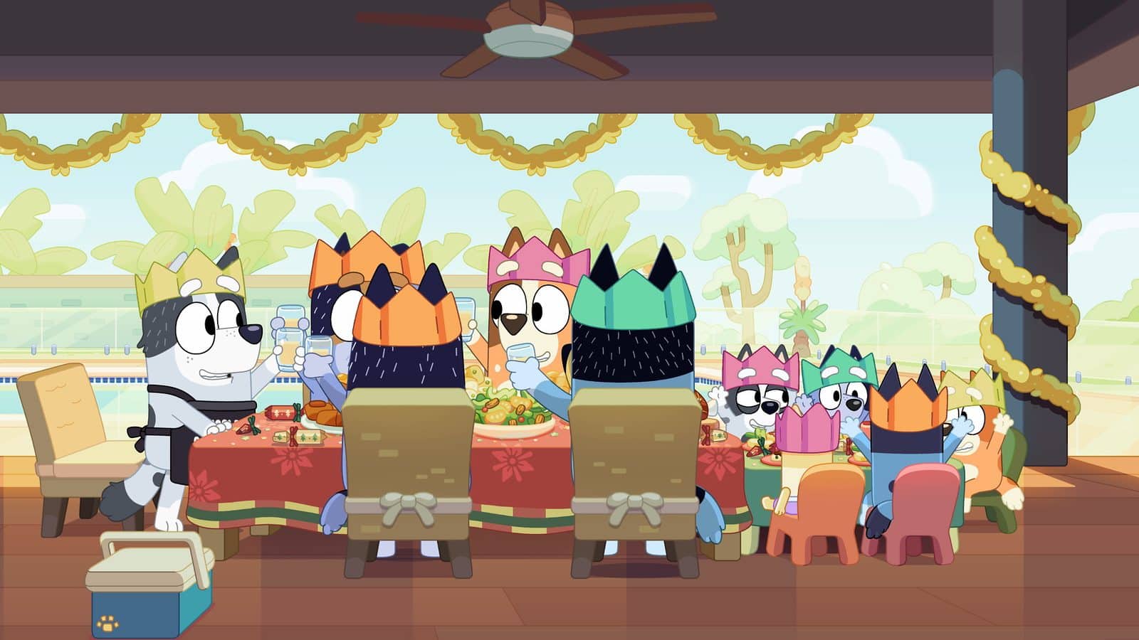 A group of cartoon dogs at a birthday feast wearing paper crowns around a table with food and drinks inside a decorated room