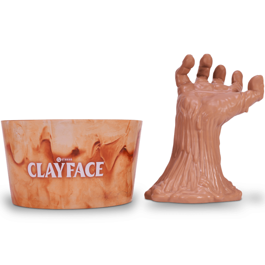 Orange marble patterned cup with the word CLAYFACE in white letters positioned beside a large brown sculpted hand reaching in from the right