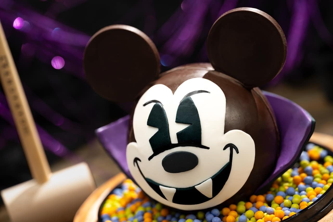 Halloween themed Mickey Mouse cake with a white face fangs and a purple cape surrounded by colorful candy beads