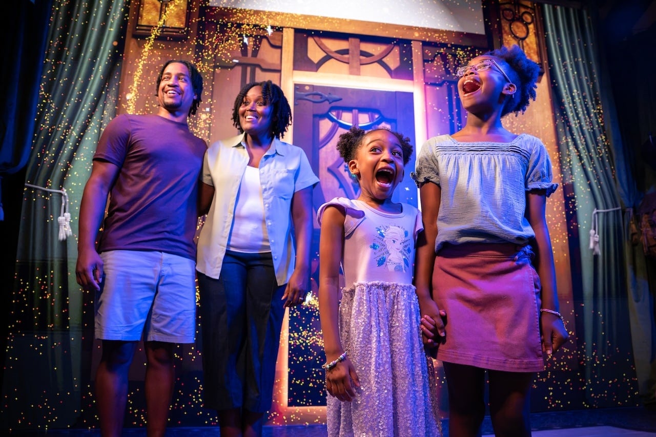 A family of four on a theater stage celebrate with confetti smiling at the audience nearby