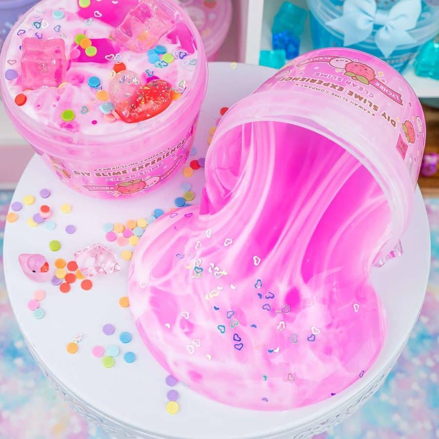 Pink slime spills from a pink jar onto a white surface topped with colorful confetti and heart shaped glitter