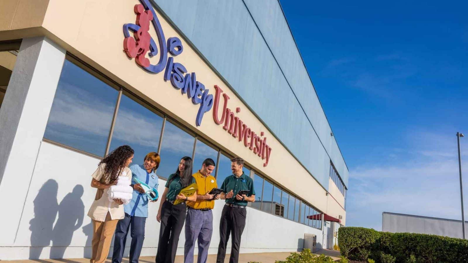 Group of diverse students stand outside a university building chatting and holding notebooks and papers against a blue sky