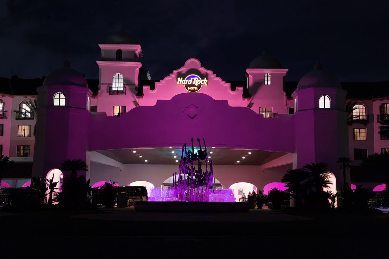 Night view of the Hard Rock Hotel with pink lighting and a lit fountain in front