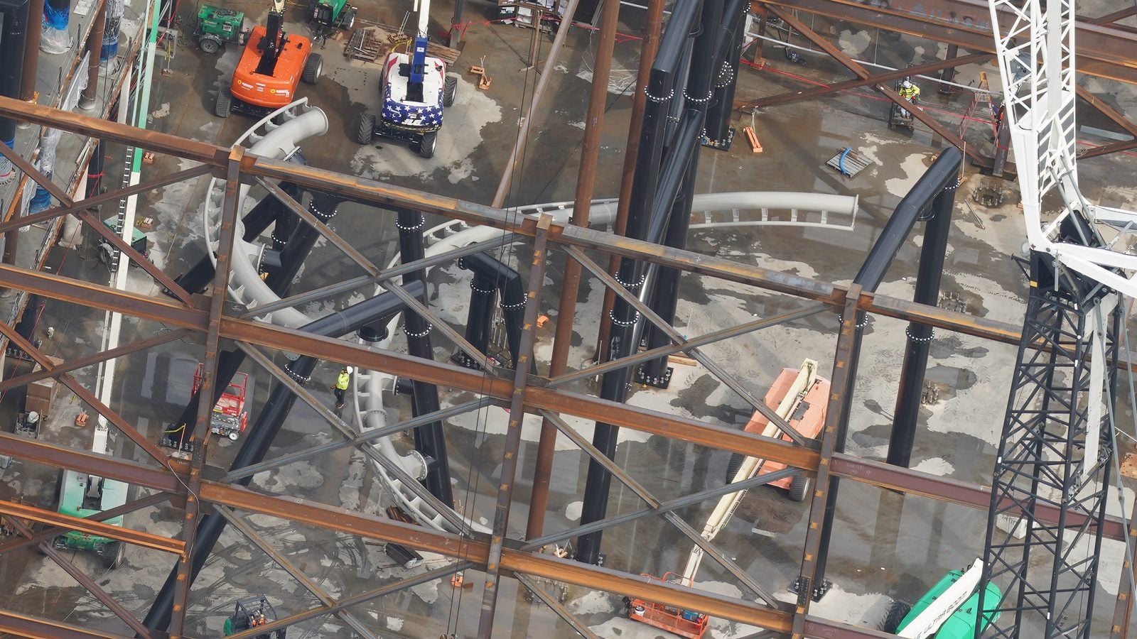 Aerial view of a construction site with intertwining steel beams cranes and workers on a wet concrete floor