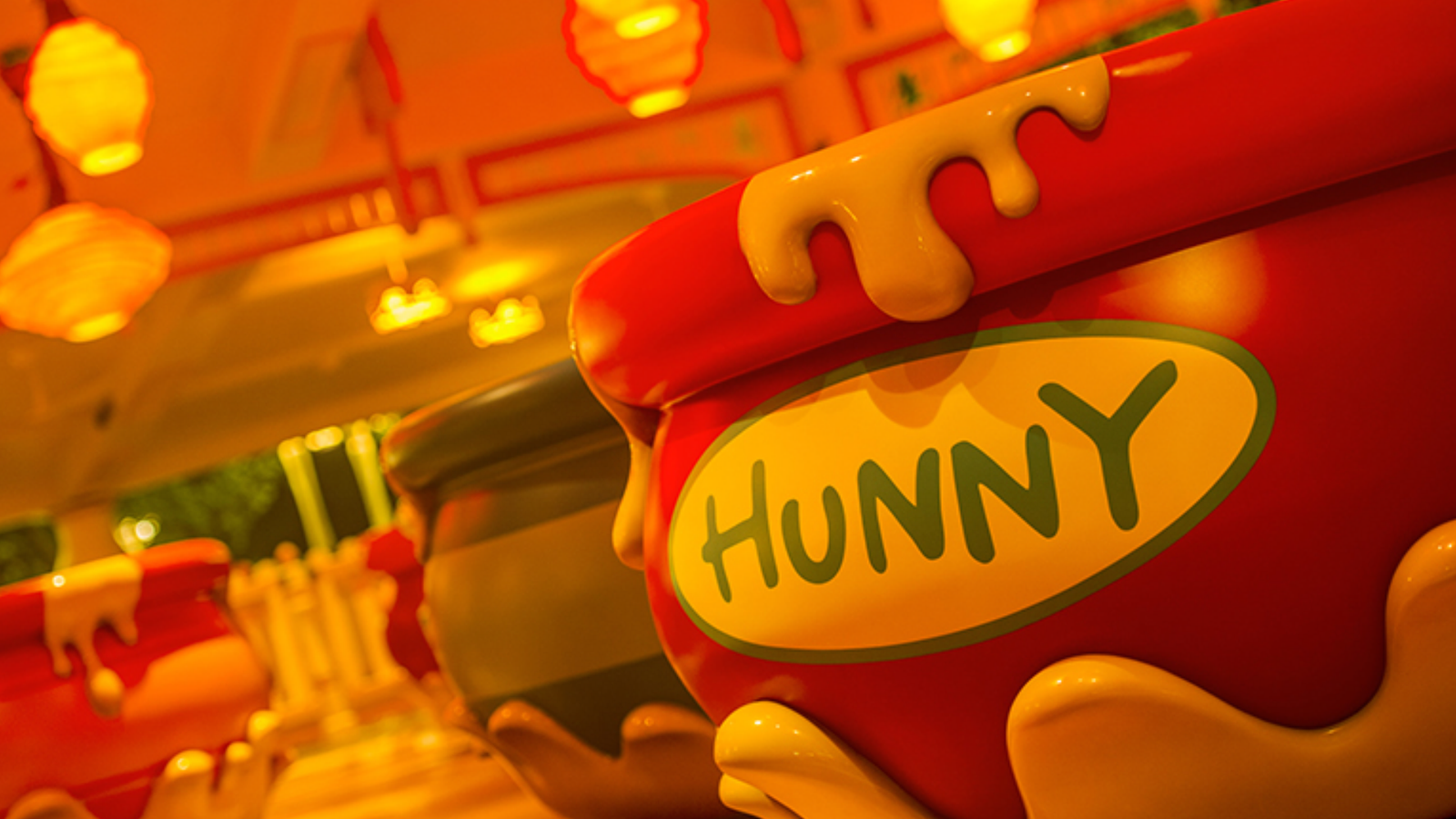 Pooh inspired red honey pot character with dripping honey and a HUNNY label set in a warm festive ride area with orange lantern lights in the background