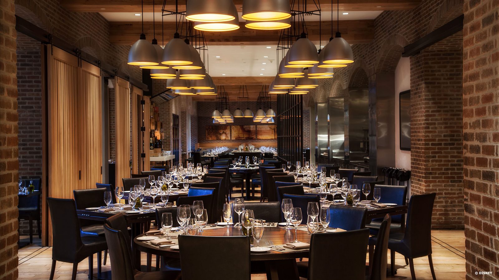 Elegant brick walled restaurant dining room with round tables set for a formal dinner under warm pendant lights