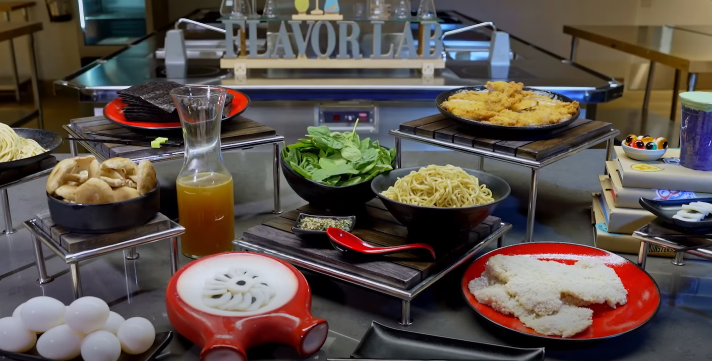 Assorted foods on metal risers in a lab style kitchen with a Flavor Lab sign in the background