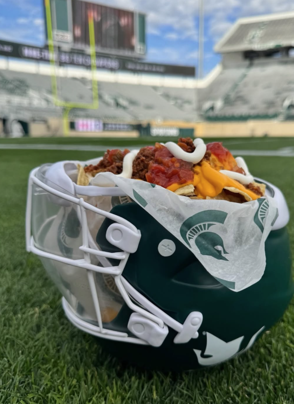 Football helmet on the grass filled with loaded nachos topped with cheese salsa and toppings in a stadium setting