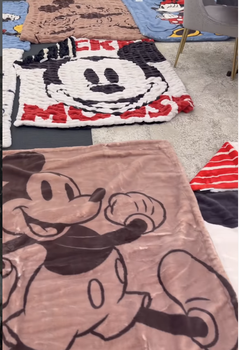 Row of colorful cartoon blankets spread on a carpet featuring Mickey Mouse and a panda