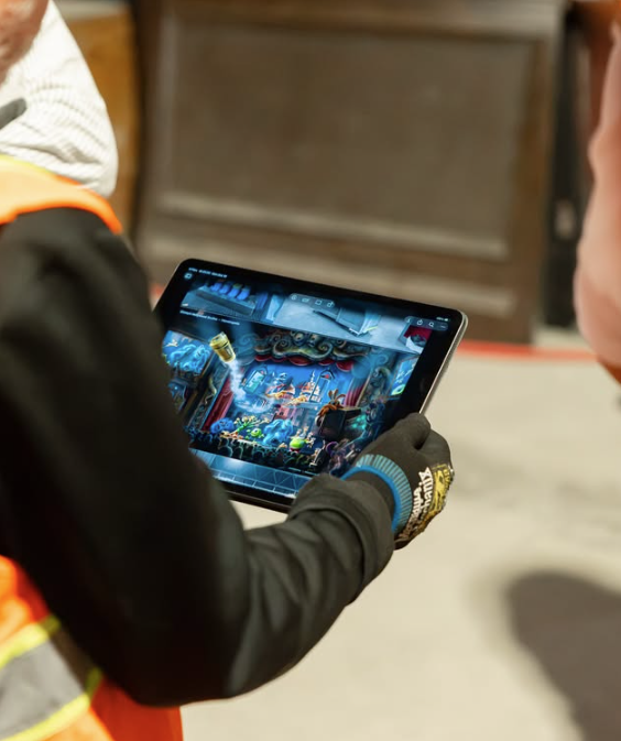 Gloved hand holding a tablet that shows a blue lit stage performance on screen