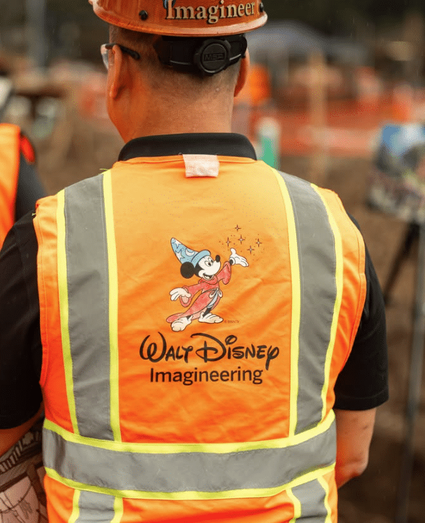Back view of a construction worker in an orange safety vest with a Mickey Mouse illustration and the Walt Disney Imagineering logo on the back