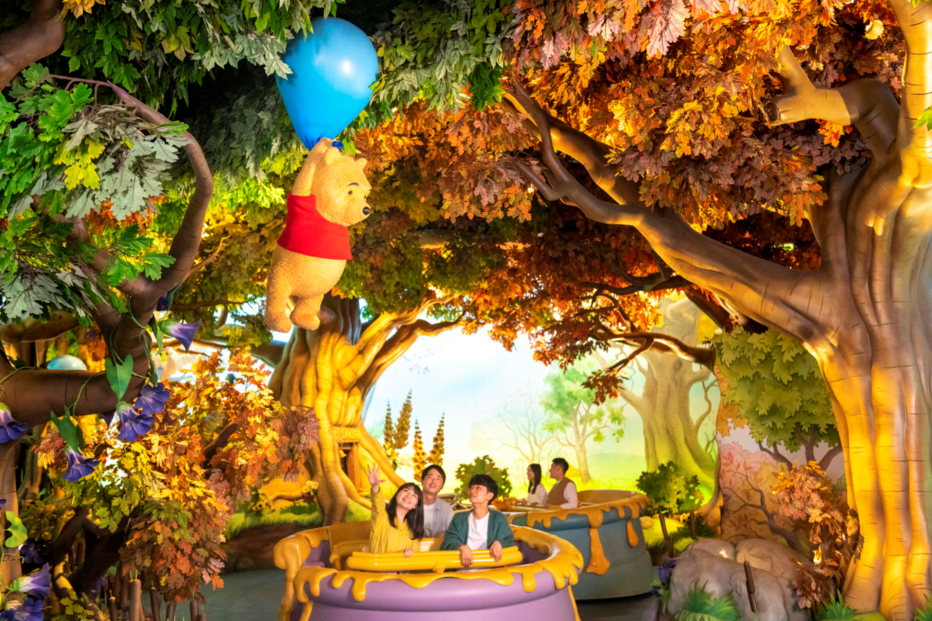 Pooh bear with a blue balloon hanging from a tree branch on a whimsical autumn themed boat ride with riders below