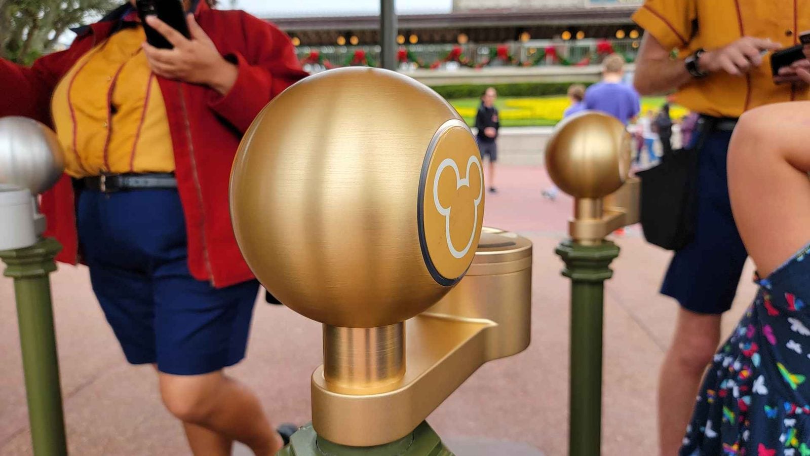 Golden turnstile with a Mickey Mouse emblem at a theme park entrance with blurred visitors in the background