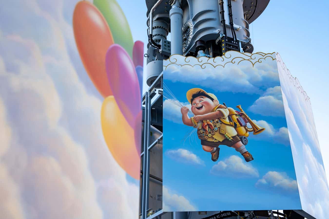 Close up of an amusement ride structure with colorful curved panels and a large banner showing a cheerful cartoon boy in a yellow outfit against a blue sky backdrop