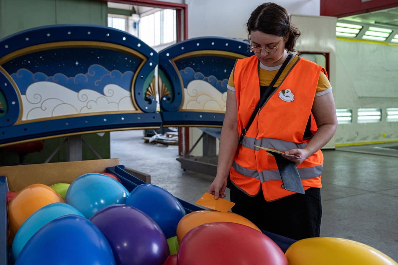 Woman in an orange high visibility vest sorting colorful balloons in a workshop setting