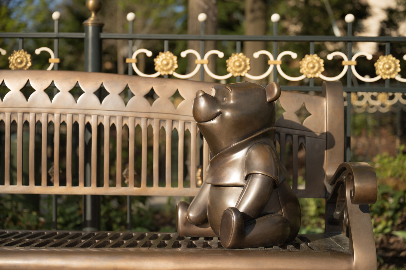 WinniethePoohParis Fantasy Land News Bronze bear statue seated on a park bench with decorative iron railing behind