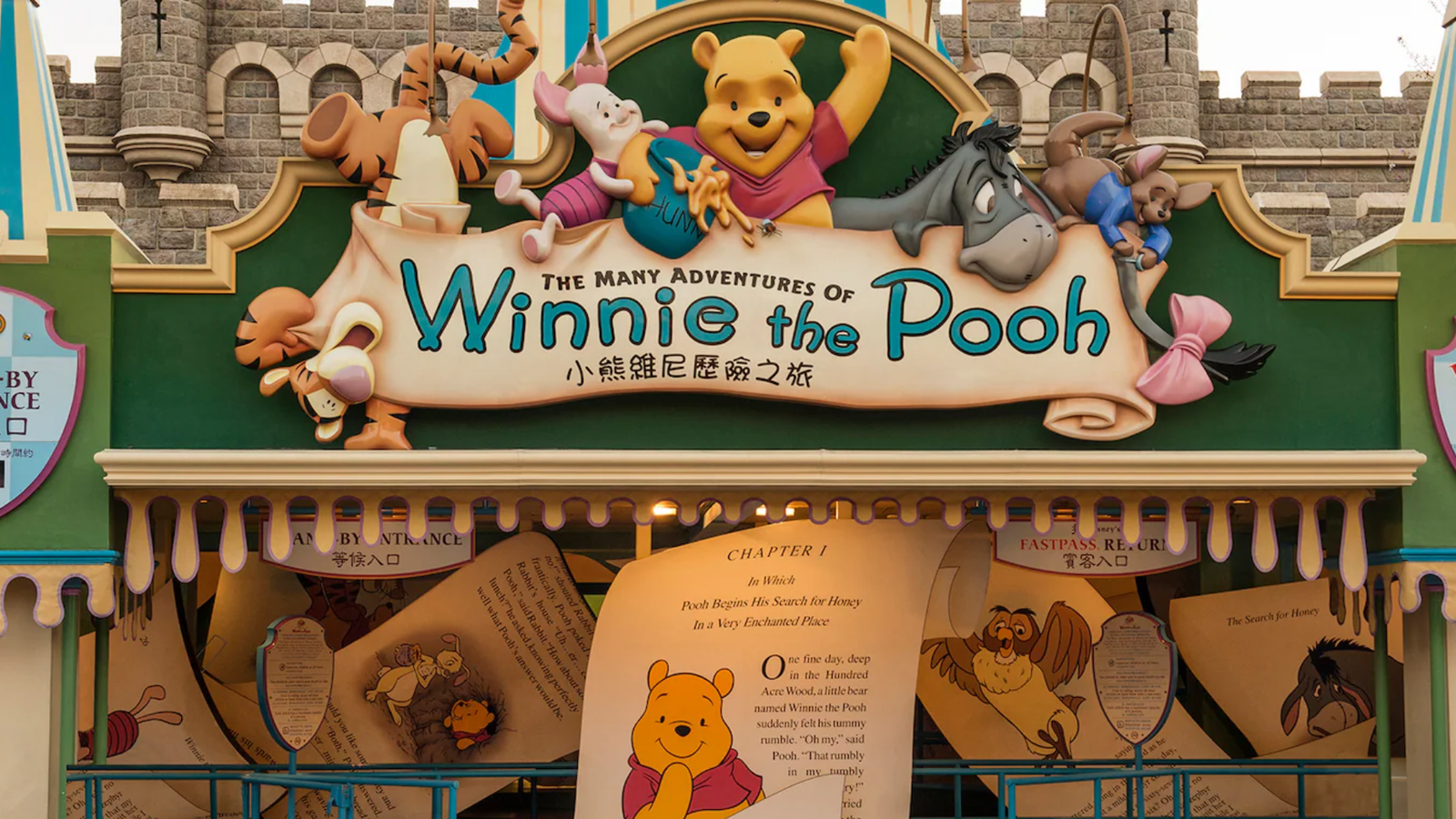 Entrance sign for The Many Adventures of Winnie the Pooh ride with Pooh waving Tigger and Piglet above and Eeyore on the right against a castle backdrop