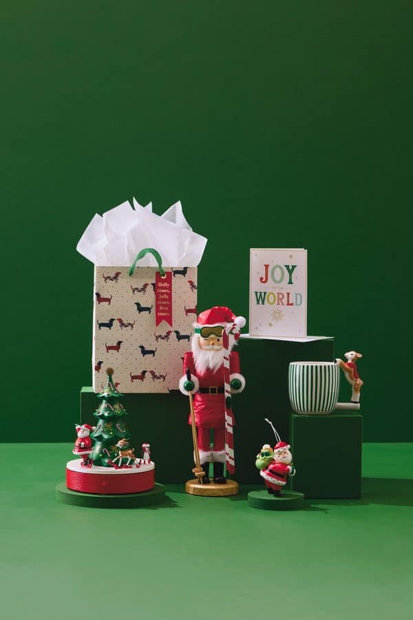 Festive holiday display with a patterned gift bag spilling white tissue a Santa figurine and a greeting card reading Joy to the World against a green backdrop