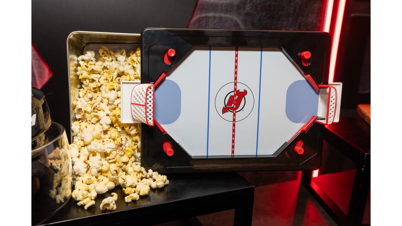 Popcorn machine at a concession stand with popcorn spilling on the left and a central hexagonal panel featuring a red logo under red lighting