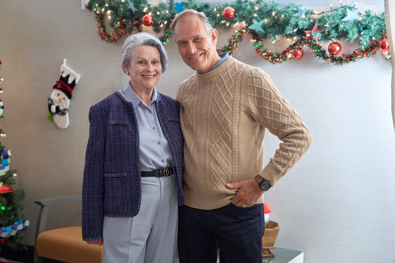 Smiling elderly couple posing together indoors with Christmas garlands and stockings in the background