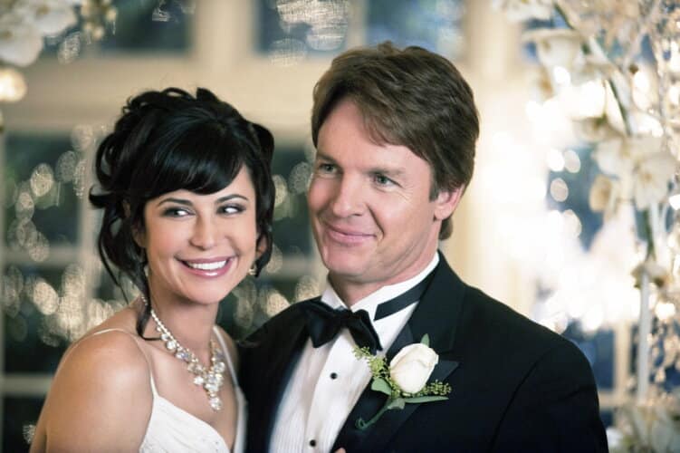 Bride and groom in wedding attire smiling together with soft background lighting behind them likely at a reception