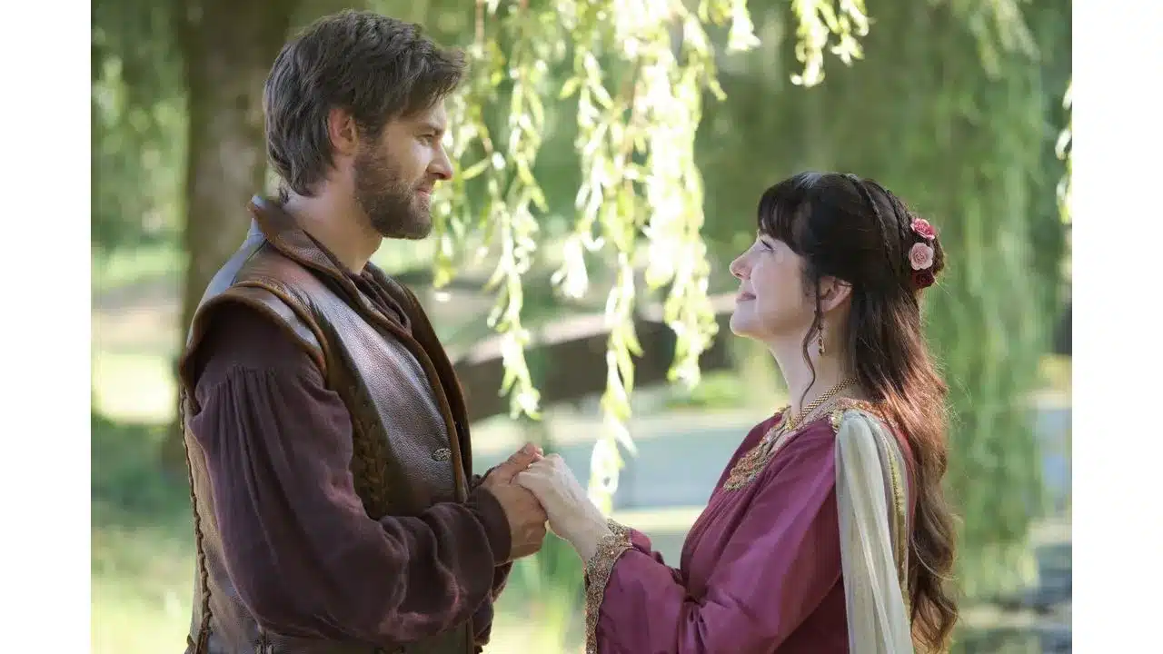 ktr1 Fantasy Land News Man and woman in medieval style outfits hold hands and smile at each other in a sunlit park like setting under hanging branches