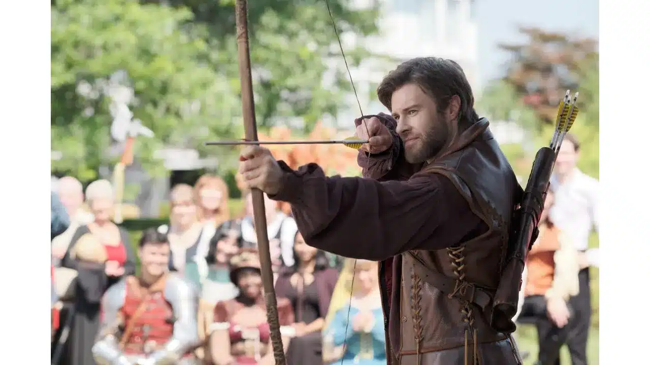ktr3 Fantasy Land News Medieval archer in leather armor drawing a longbow at an outdoor festival with a crowd watching in the background