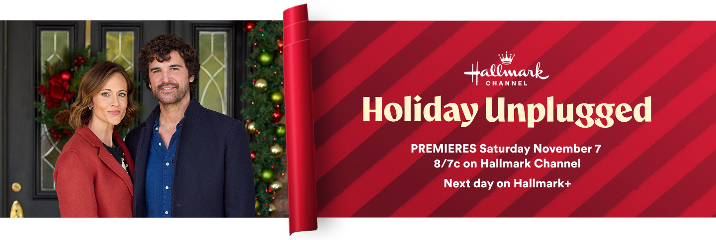 Two people stand at a festive front door beside a rolled red banner that reads Holiday Unplugged on Hallmark Channel