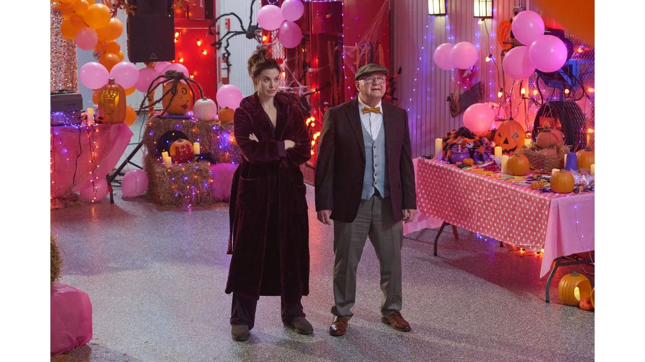 spiritofhalloween1 Fantasy Land News Two adults in costume stand in a Halloween party scene with pumpkins pink balloons and string lights behind them