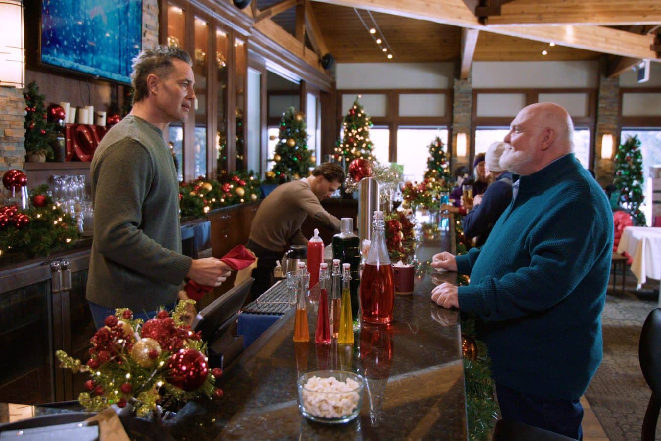 Two men chat at a holiday decorated bar with Christmas trees and colorful bottles on the counter'Tis the Season for Setups Review: Hallmark Kicks Off Countdown to Christmas 2026